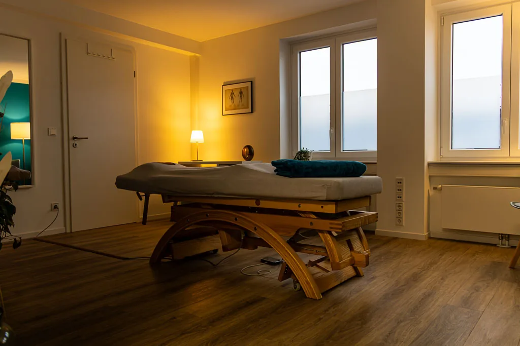 Behandlungsraum des Therapiezentrums Barop mit Holzliege, Stehlampe und Anatomiebild