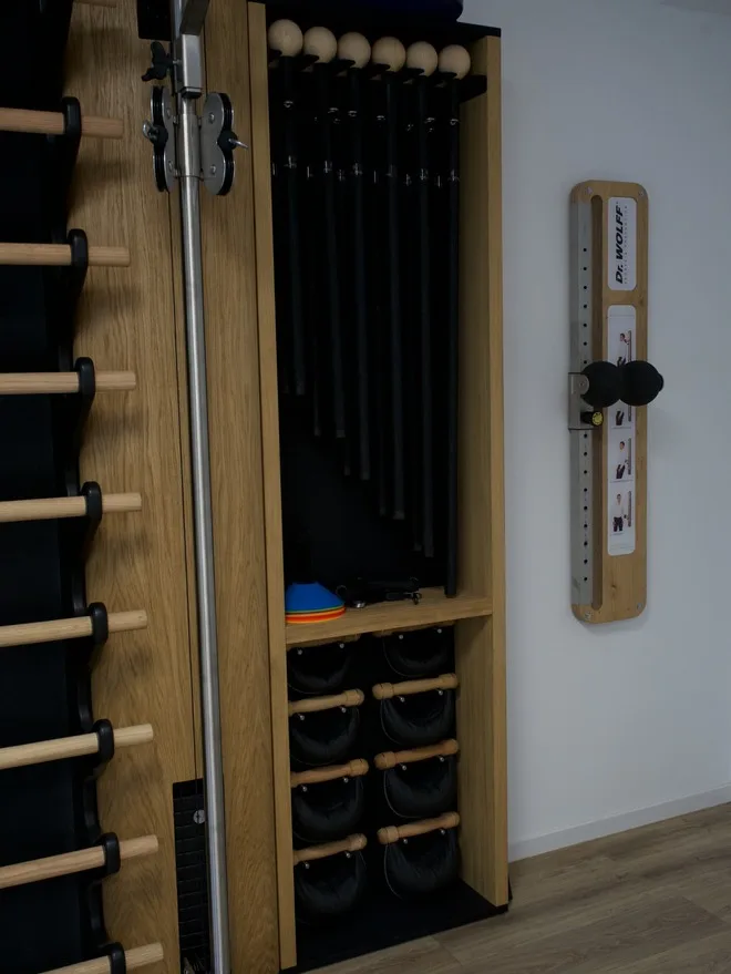 Sprossenwand mit Seilzug, daneben ein Regal mit Trainingsstangen und Gewichten